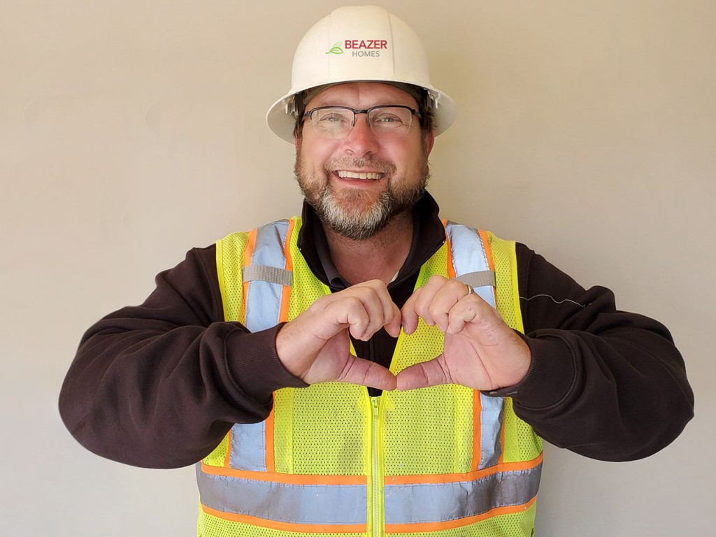Beazer employee in safety vest and hard hat making a heart with his hands