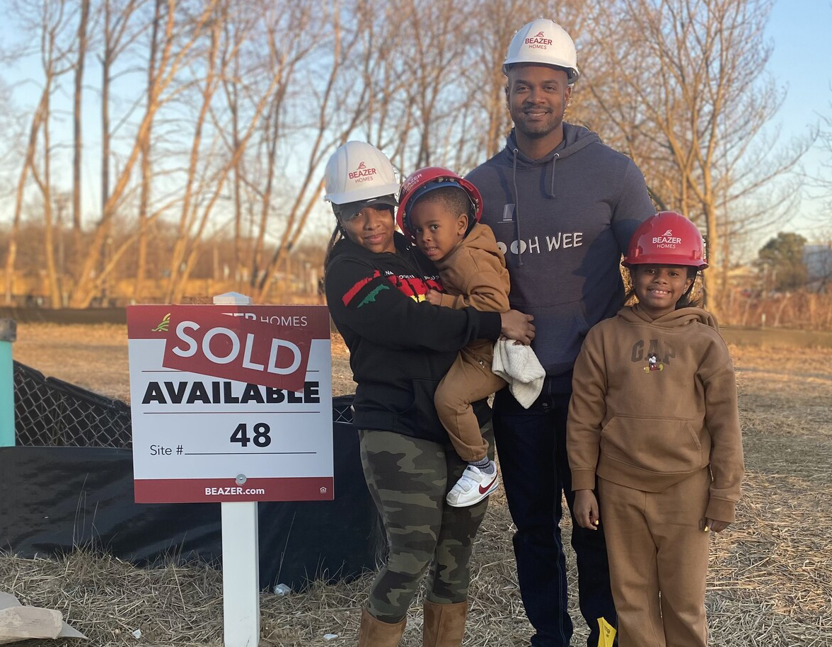 Family standing next to sold sign on their empty lot